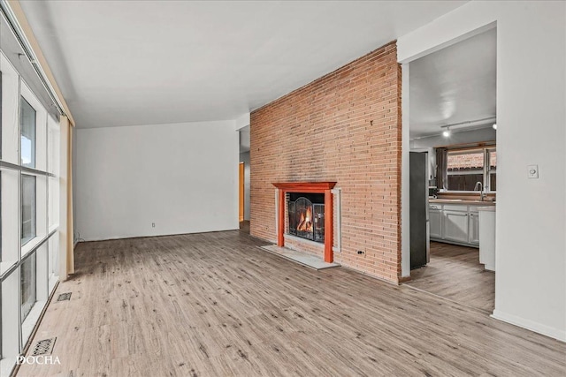 unfurnished living room with a fireplace, light hardwood / wood-style flooring, brick wall, and sink