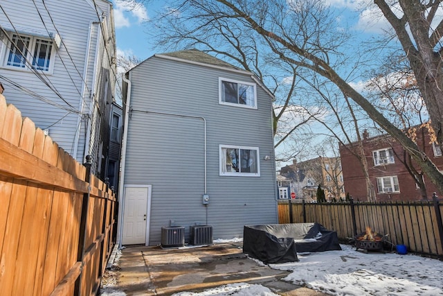 snow covered rear of property featuring central AC unit and an outdoor fire pit