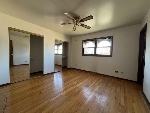 unfurnished bedroom with ceiling fan, wood-type flooring, and two closets