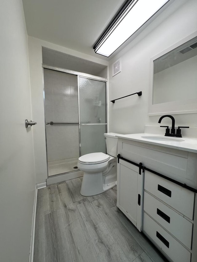 bathroom featuring vanity, wood-type flooring, a shower with shower door, and toilet