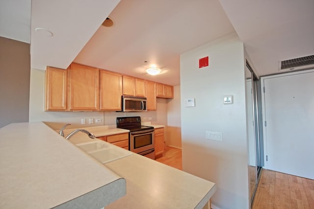 kitchen with kitchen peninsula, appliances with stainless steel finishes, sink, light brown cabinets, and light hardwood / wood-style floors