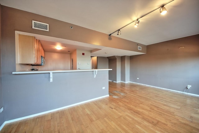 kitchen featuring a kitchen bar, kitchen peninsula, light hardwood / wood-style flooring, and track lighting