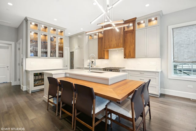 kitchen with white cabinetry, sink, dark hardwood / wood-style floors, a kitchen island with sink, and a breakfast bar