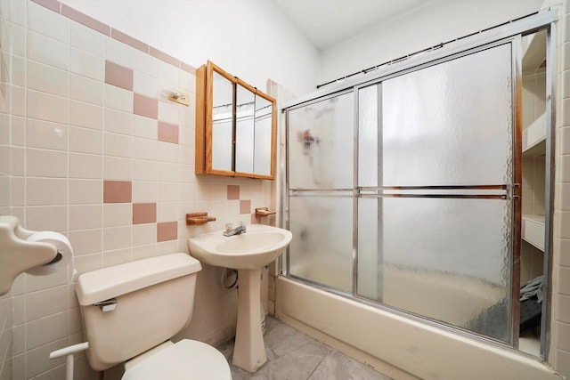 bathroom with tile patterned floors, toilet, combined bath / shower with glass door, and tile walls