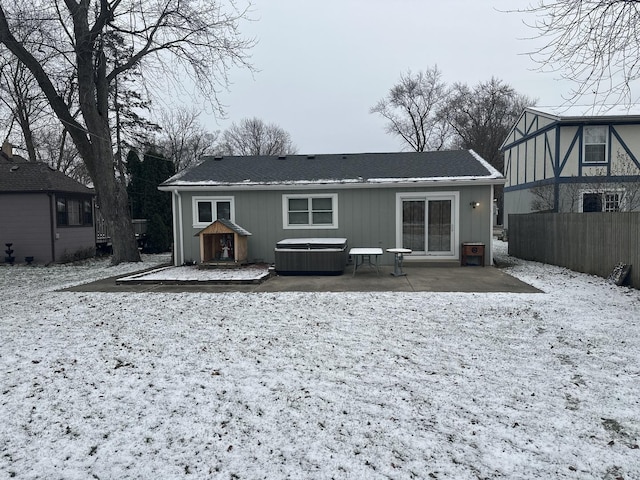 snow covered rear of property with a patio area and a hot tub