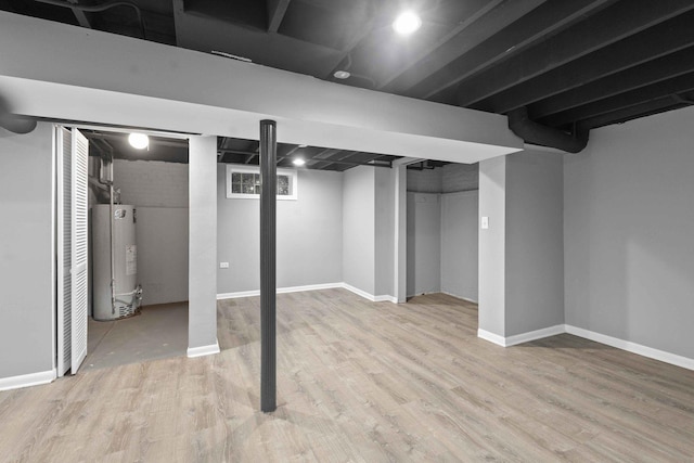 basement with light hardwood / wood-style floors and water heater