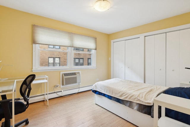 bedroom featuring an AC wall unit, a baseboard heating unit, multiple closets, and light hardwood / wood-style floors