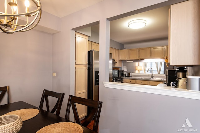 kitchen with kitchen peninsula, light brown cabinetry, stainless steel appliances, sink, and an inviting chandelier