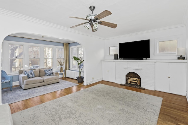 unfurnished living room with crown molding, a brick fireplace, dark wood-type flooring, and ceiling fan