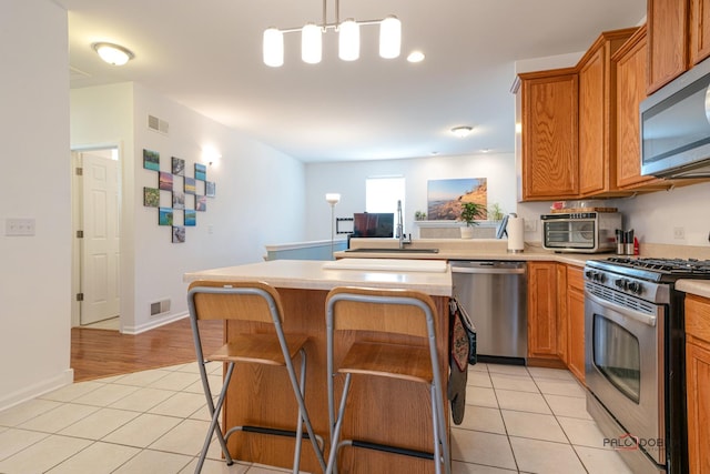 kitchen featuring a kitchen bar, sink, hanging light fixtures, stainless steel appliances, and light tile patterned floors