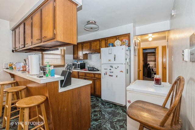 kitchen featuring tasteful backsplash, kitchen peninsula, white fridge, and a breakfast bar area