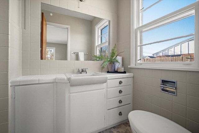 bathroom with toilet, vanity, and tile walls