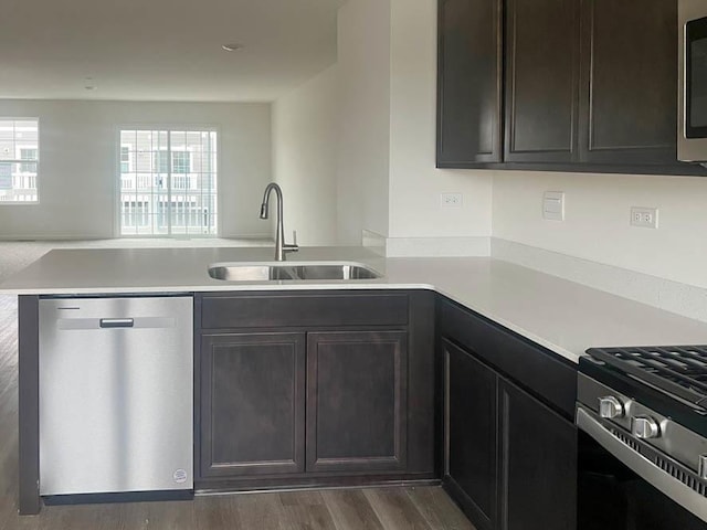 kitchen with dark wood-type flooring, kitchen peninsula, sink, appliances with stainless steel finishes, and dark brown cabinetry