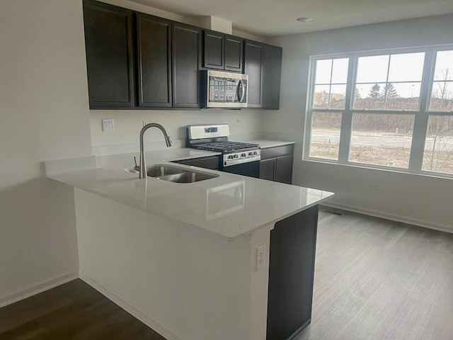 kitchen with light stone countertops, sink, stainless steel appliances, light hardwood / wood-style flooring, and kitchen peninsula