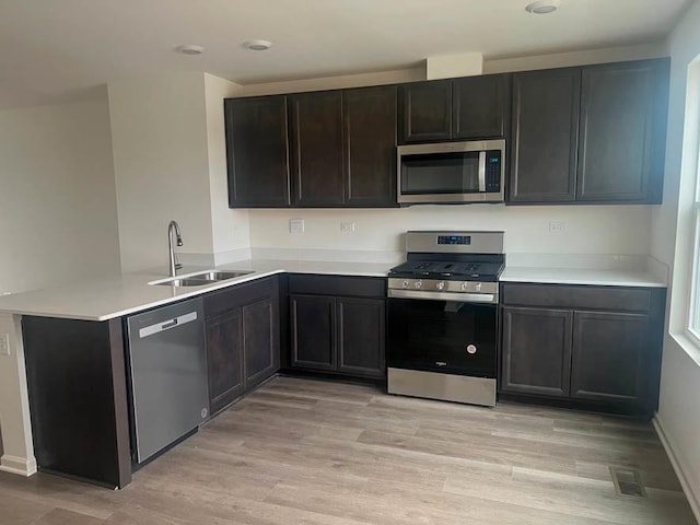 kitchen featuring kitchen peninsula, sink, light hardwood / wood-style floors, and appliances with stainless steel finishes