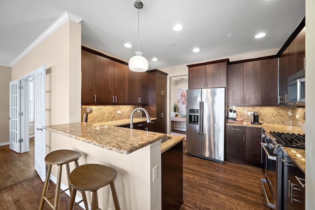 kitchen with appliances with stainless steel finishes, a breakfast bar area, hanging light fixtures, dark brown cabinetry, and kitchen peninsula