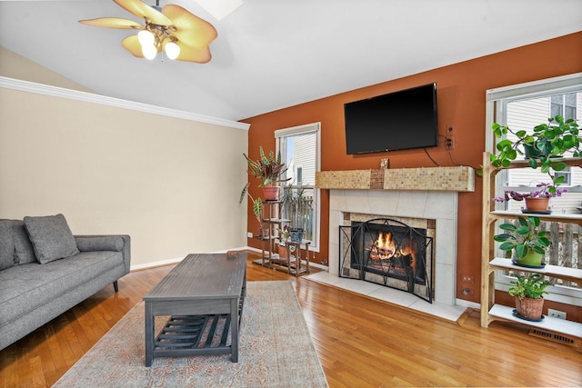 living room with a tile fireplace, ceiling fan, wood-type flooring, and vaulted ceiling