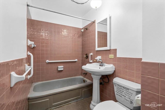 bathroom with tile patterned flooring, tiled shower / bath combo, toilet, and tile walls