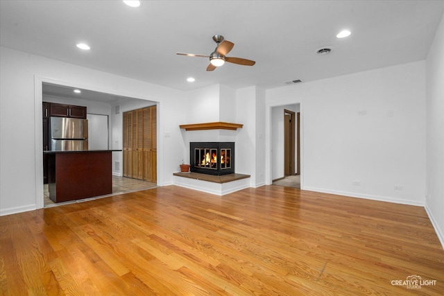 unfurnished living room featuring ceiling fan, light hardwood / wood-style floors, and a multi sided fireplace