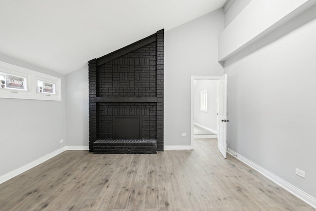 unfurnished living room with a brick fireplace, light hardwood / wood-style flooring, and lofted ceiling