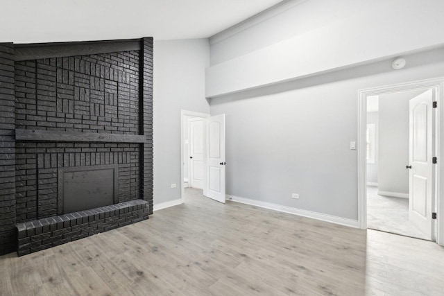 unfurnished living room featuring light hardwood / wood-style flooring, a towering ceiling, and a brick fireplace