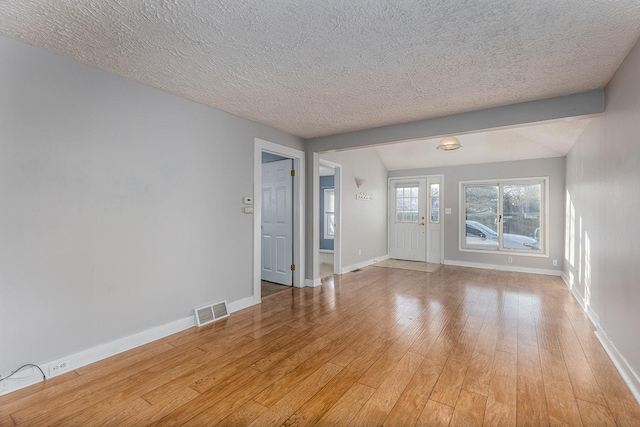 unfurnished living room with beamed ceiling, a textured ceiling, and light hardwood / wood-style flooring