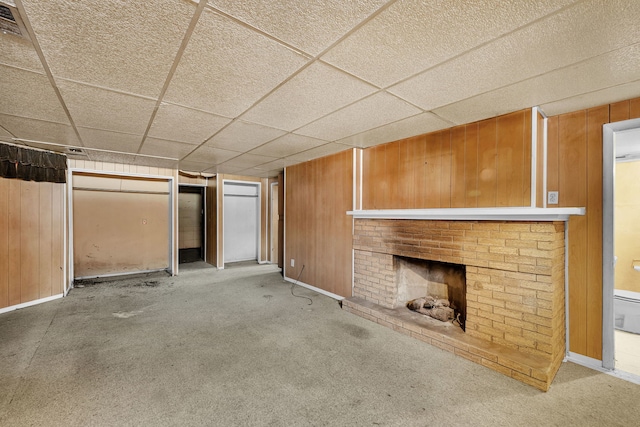 unfurnished living room with carpet flooring, wooden walls, a fireplace, and a drop ceiling