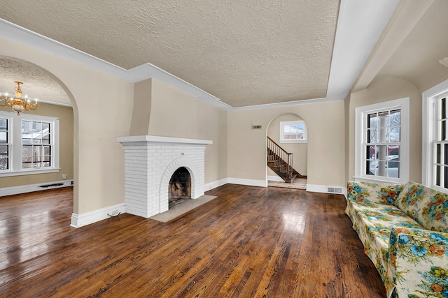 unfurnished living room featuring dark wood-type flooring, a brick fireplace, ornamental molding, a textured ceiling, and a chandelier