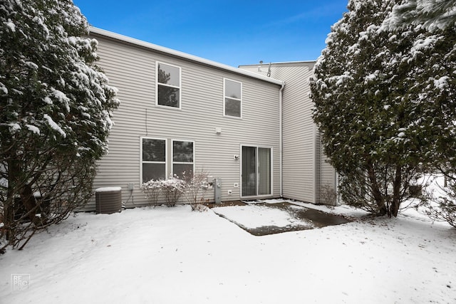 snow covered rear of property featuring central AC