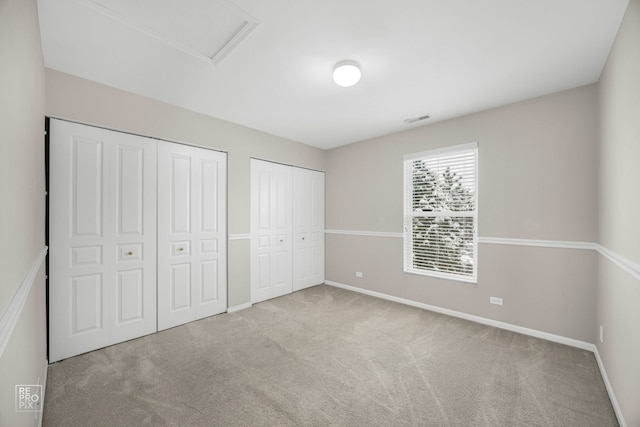 unfurnished bedroom featuring light colored carpet and multiple closets