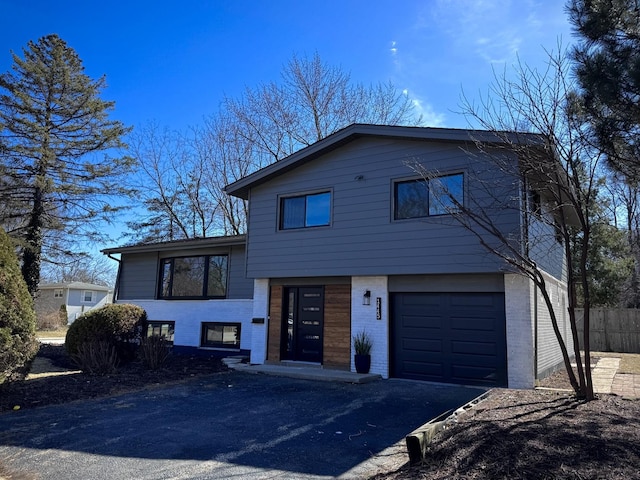 split level home featuring a garage, brick siding, driveway, and fence