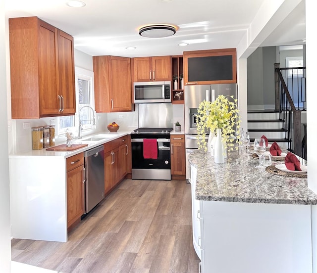 kitchen featuring light wood-type flooring, light stone counters, appliances with stainless steel finishes, brown cabinetry, and a sink