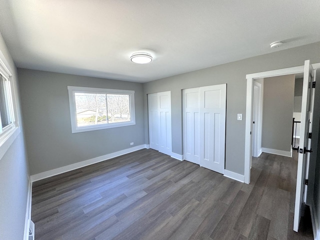 unfurnished bedroom featuring baseboards, multiple closets, and dark wood-style flooring