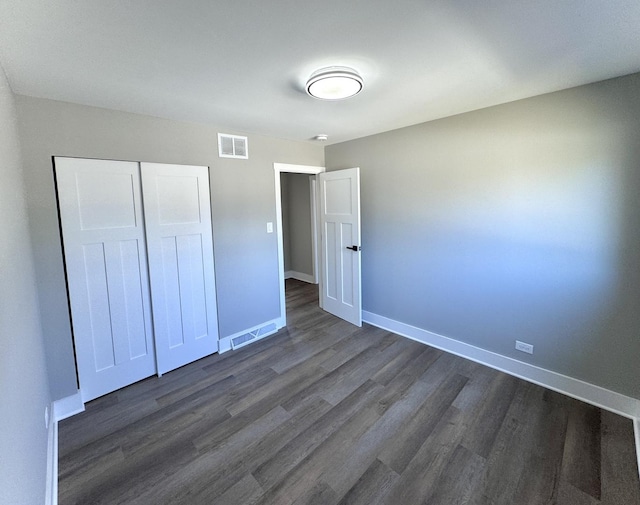 unfurnished bedroom featuring visible vents, baseboards, dark wood-type flooring, and a closet