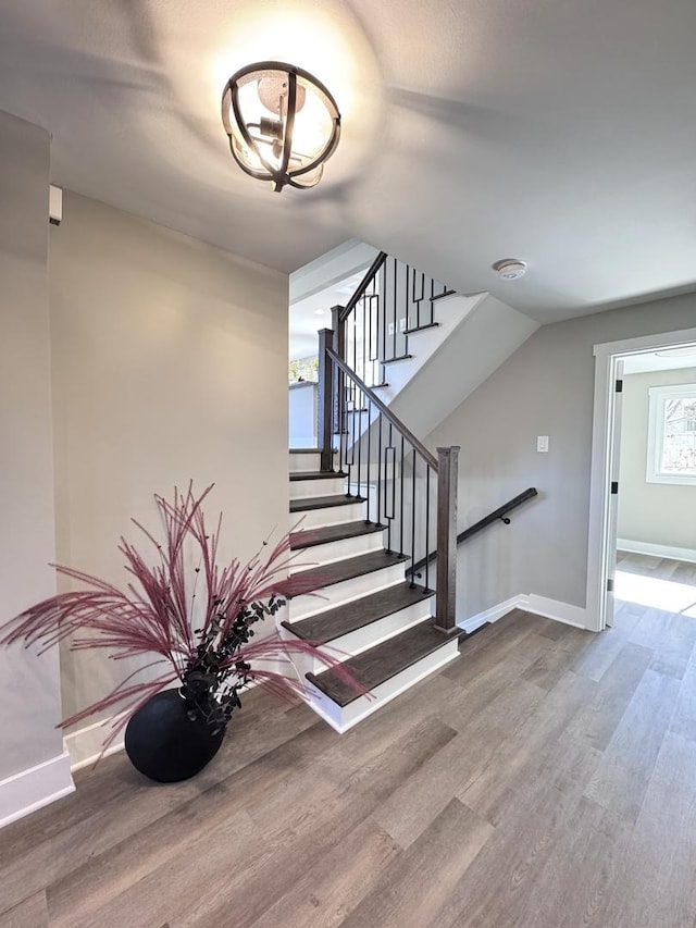 staircase featuring a chandelier, baseboards, wood finished floors, and vaulted ceiling