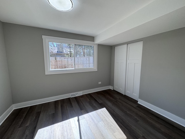 unfurnished bedroom featuring visible vents, baseboards, a closet, and dark wood finished floors