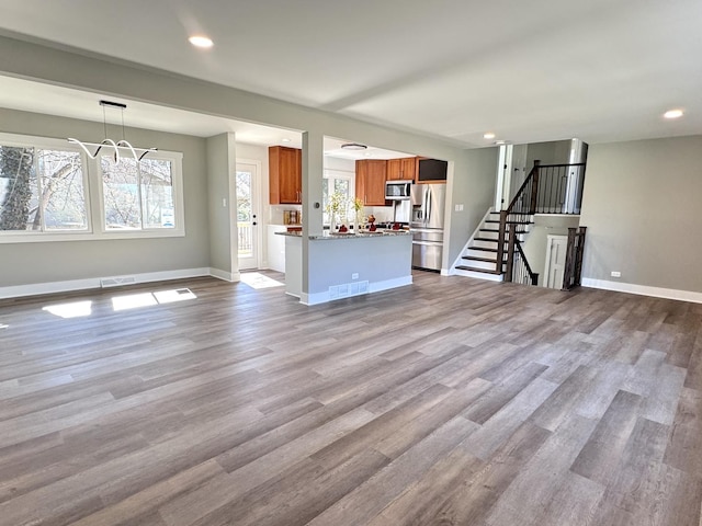 unfurnished living room featuring visible vents, baseboards, wood finished floors, and stairway