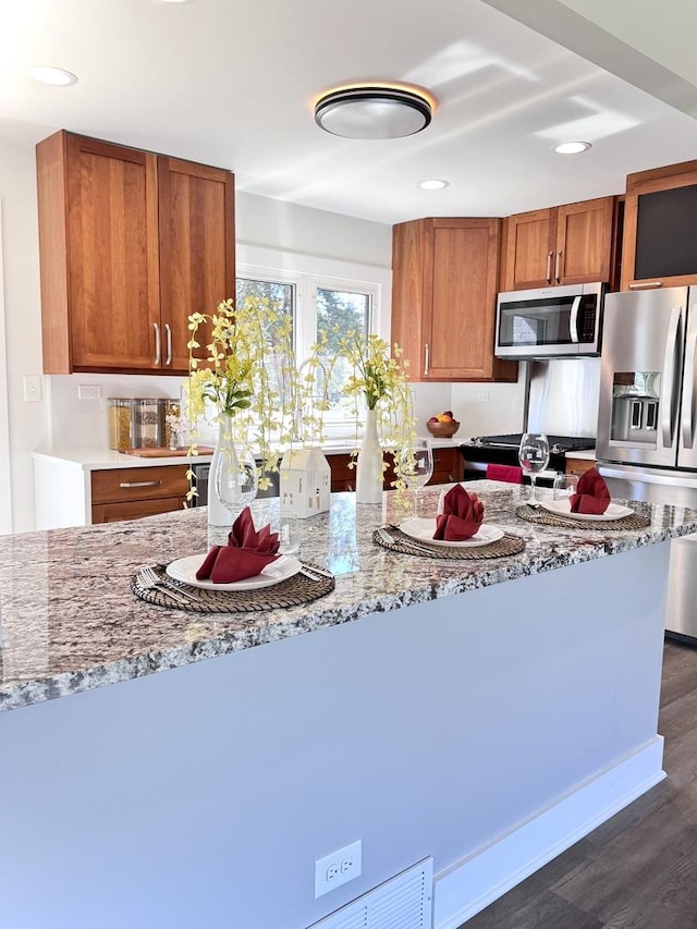 kitchen featuring light stone countertops, dark wood-style floors, recessed lighting, brown cabinetry, and stainless steel appliances