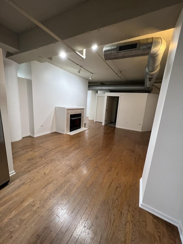 basement with rail lighting, hardwood / wood-style flooring, and a tiled fireplace