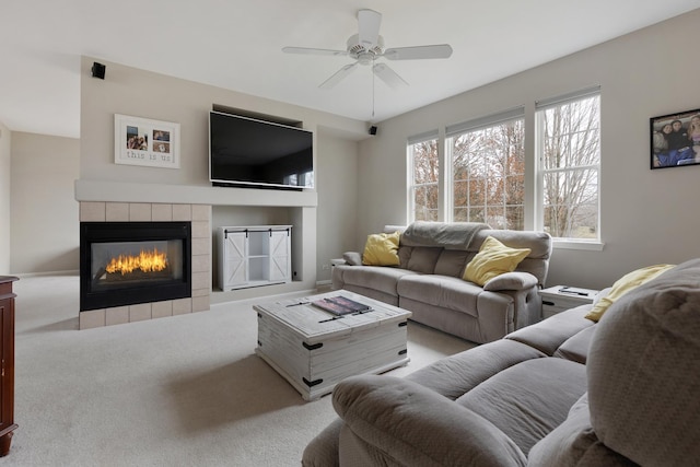 living room featuring a tiled fireplace, ceiling fan, and light carpet