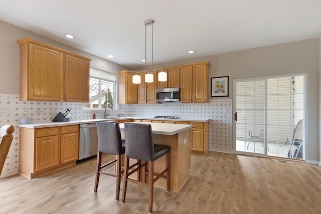 kitchen featuring sink, hanging light fixtures, appliances with stainless steel finishes, a kitchen island, and light wood-type flooring