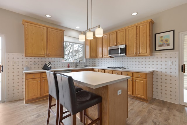 kitchen featuring sink, a center island, gas stovetop, pendant lighting, and light hardwood / wood-style floors