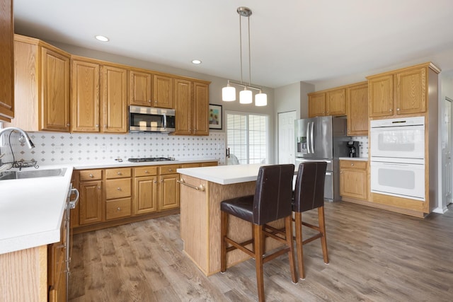 kitchen with appliances with stainless steel finishes, sink, light hardwood / wood-style flooring, a kitchen island, and hanging light fixtures