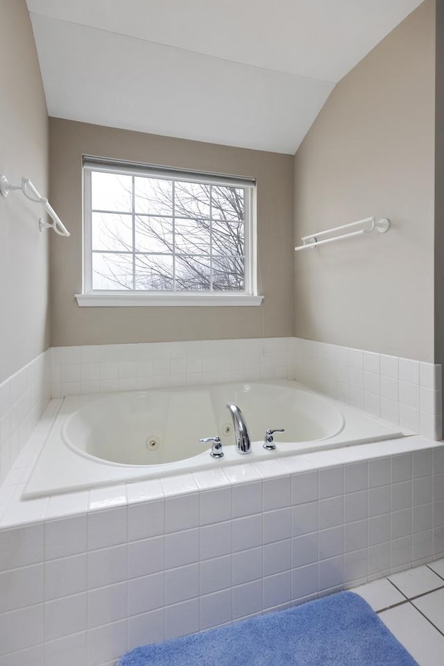 bathroom with tile patterned flooring, vaulted ceiling, and tiled tub