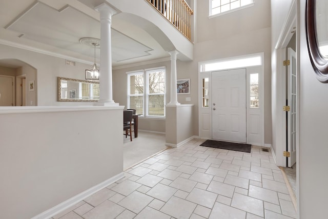 tiled foyer featuring decorative columns, a towering ceiling, a chandelier, and ornamental molding