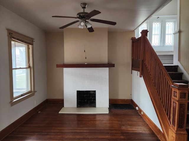 unfurnished living room featuring ceiling fan, plenty of natural light, dark hardwood / wood-style floors, and a brick fireplace