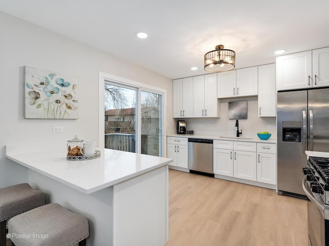 kitchen with kitchen peninsula, a kitchen breakfast bar, stainless steel appliances, light hardwood / wood-style floors, and white cabinetry