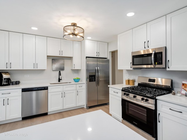 kitchen featuring appliances with stainless steel finishes, sink, light hardwood / wood-style flooring, a notable chandelier, and white cabinetry