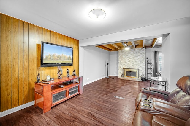 living room with wood walls, a fireplace, beamed ceiling, and dark wood-type flooring