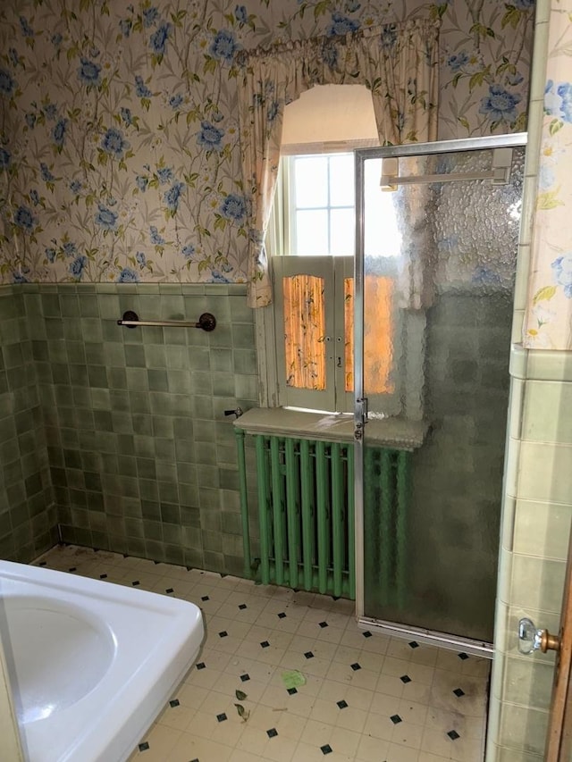 bathroom featuring a shower with shower door, radiator heating unit, and tile walls